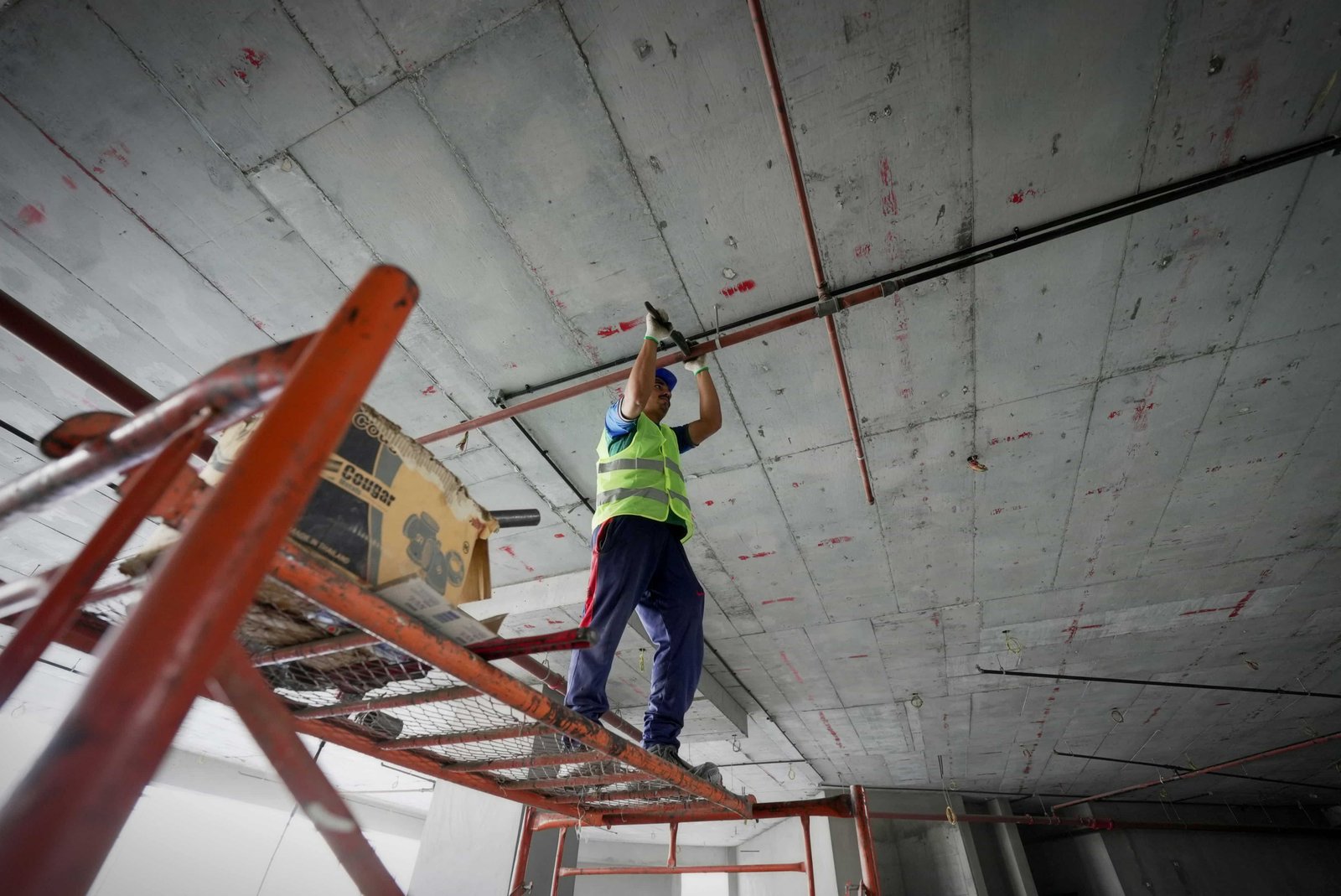 Construction worker on scaffolding installing ceiling piping inside a commercial building.