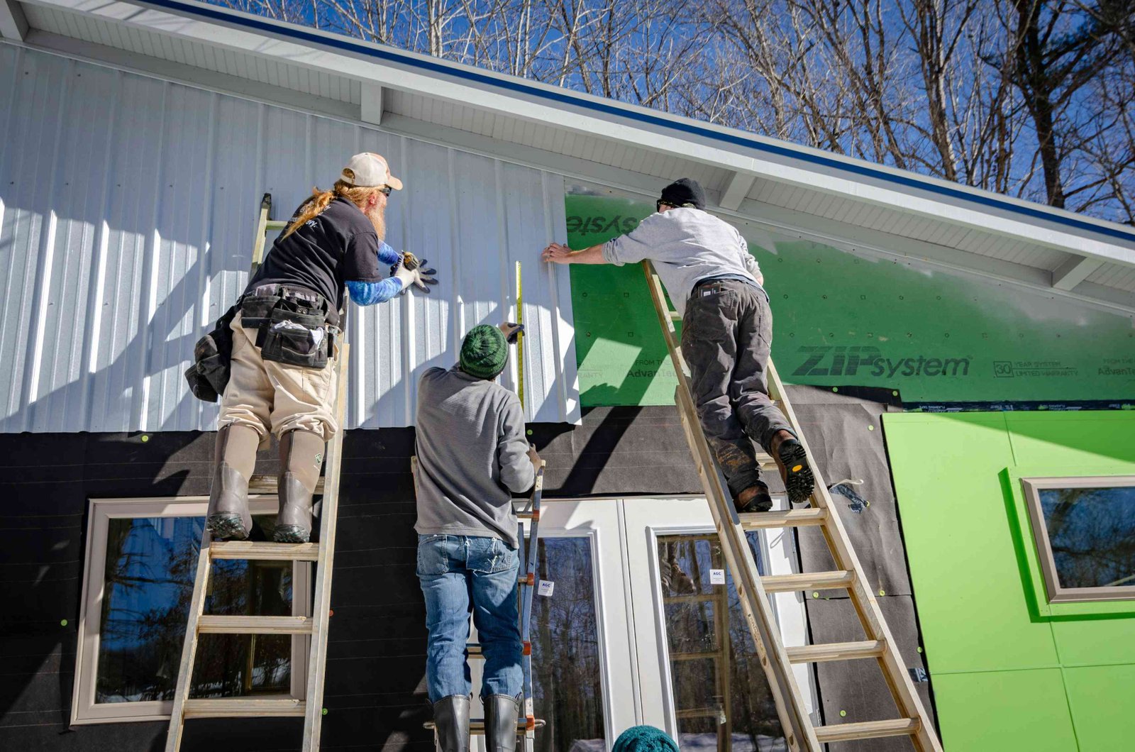 Three construction workers installing exterior siding on a house during renovation.