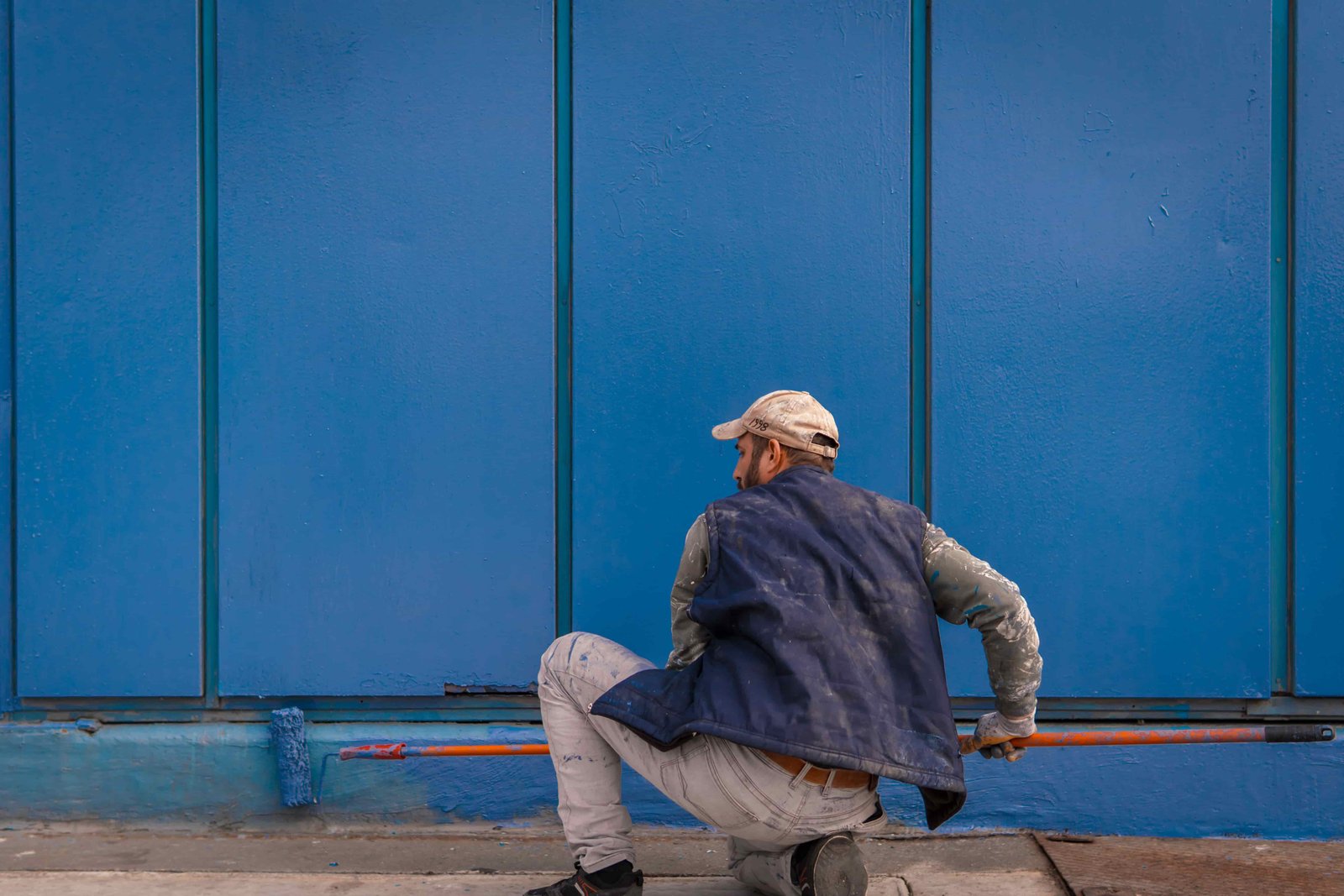 Worker painting the lower exterior wall of a commercial building with a paint roller.