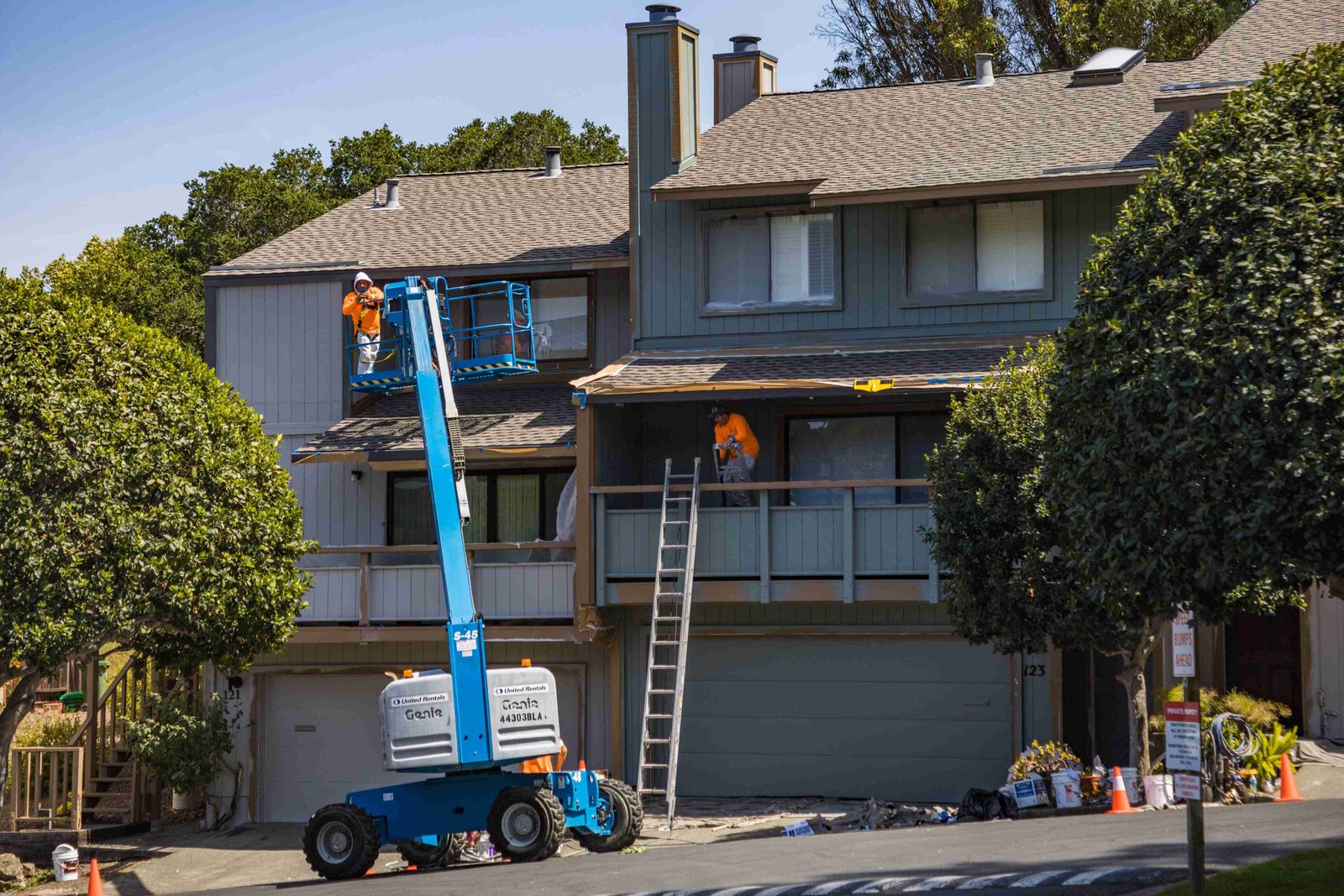 Construction workers using a boom lift and ladder during an exterior townhouse renovation.